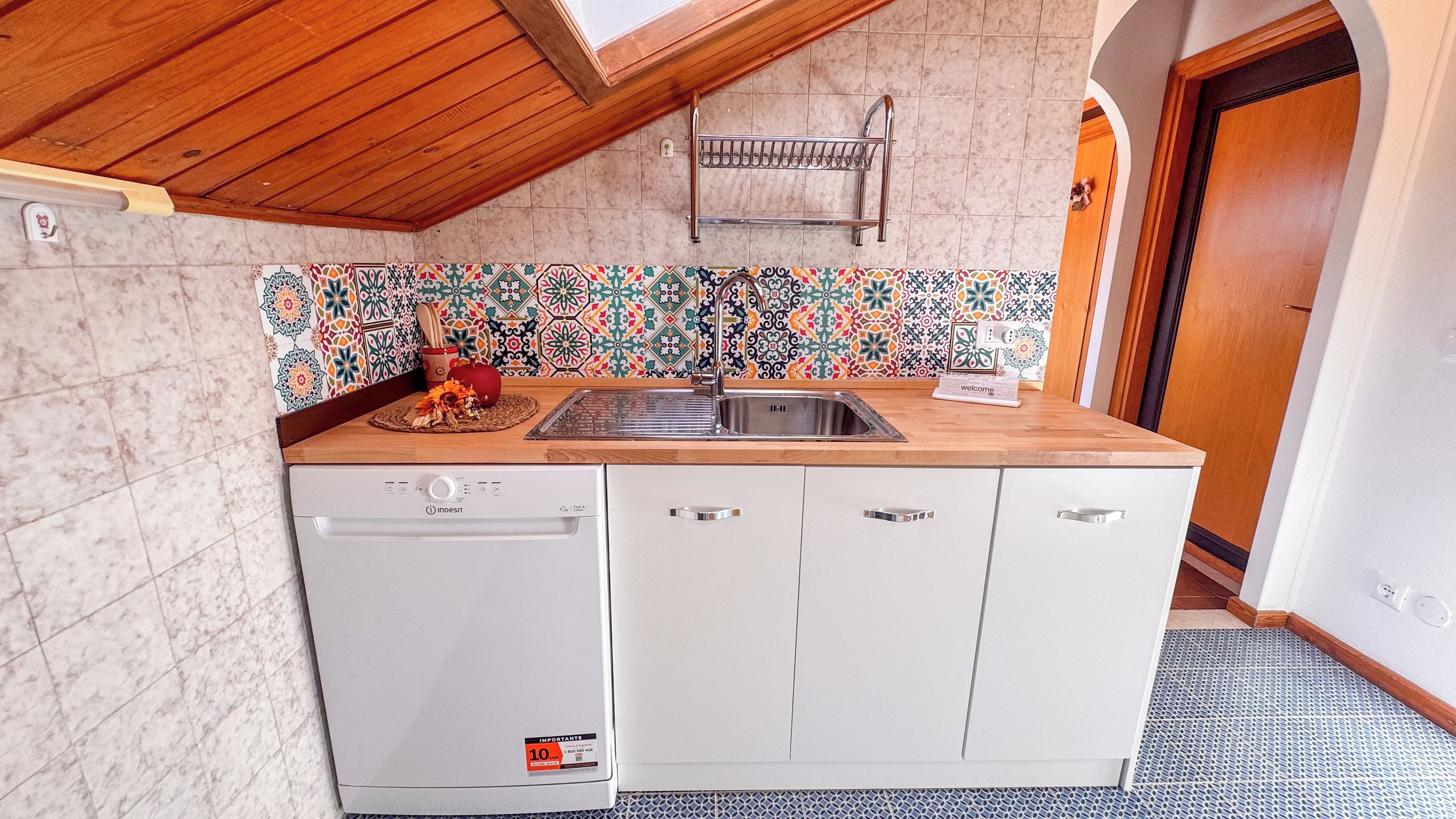 A compact kitchen with a dishwasher, a sink, and a tiled backsplash.