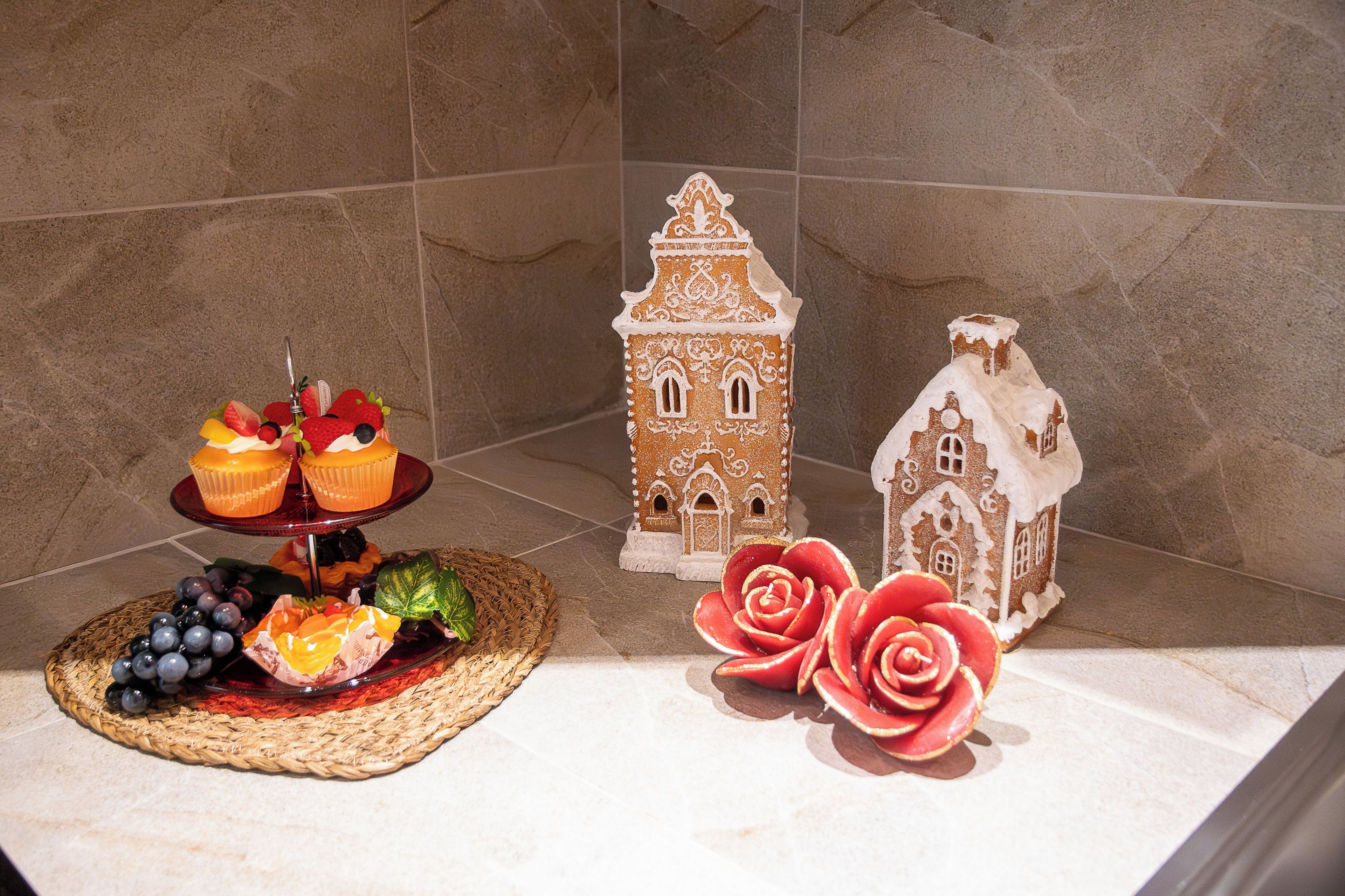 A kitchen counter with a fruit platter, two gingerbread houses, and decorative roses.
