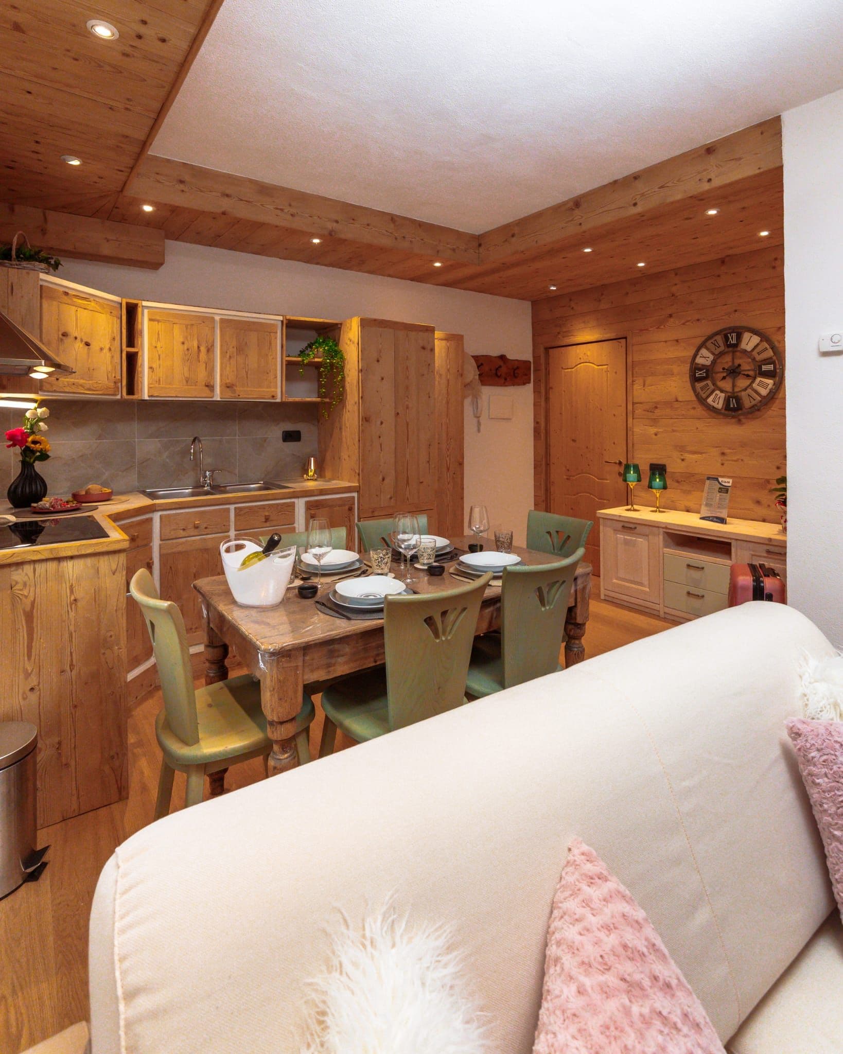 Une cuisine chaleureuse avec des meubles en bois, une table à manger pour quatre personnes et une horloge au mur.