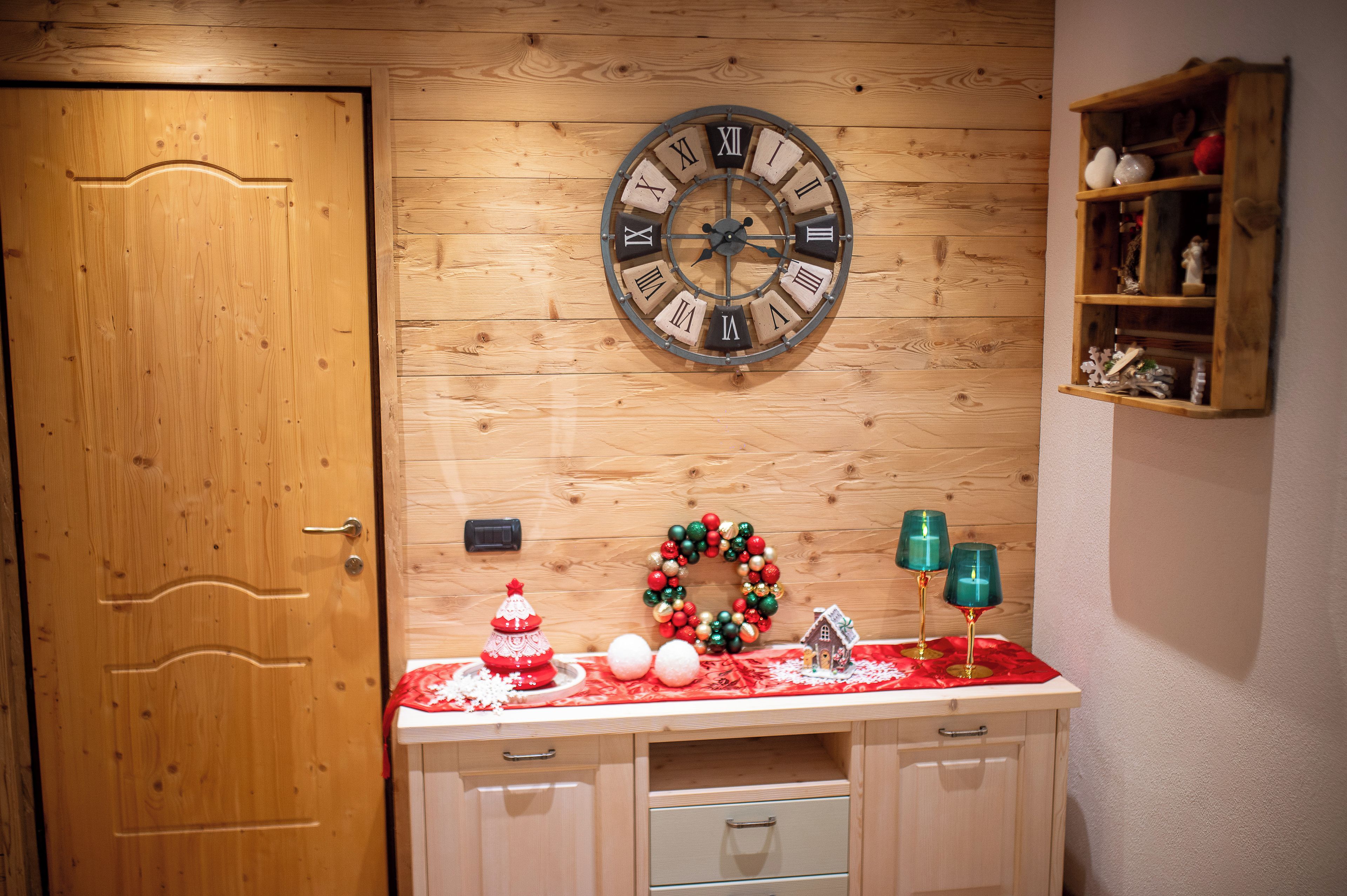 A wooden wall with a large clock, a wooden door, and a shelf with decorative items.
