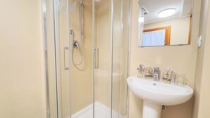 Un baño con ducha envuelta en vidrio, un lavamanos blanco y un espejo sobre él.