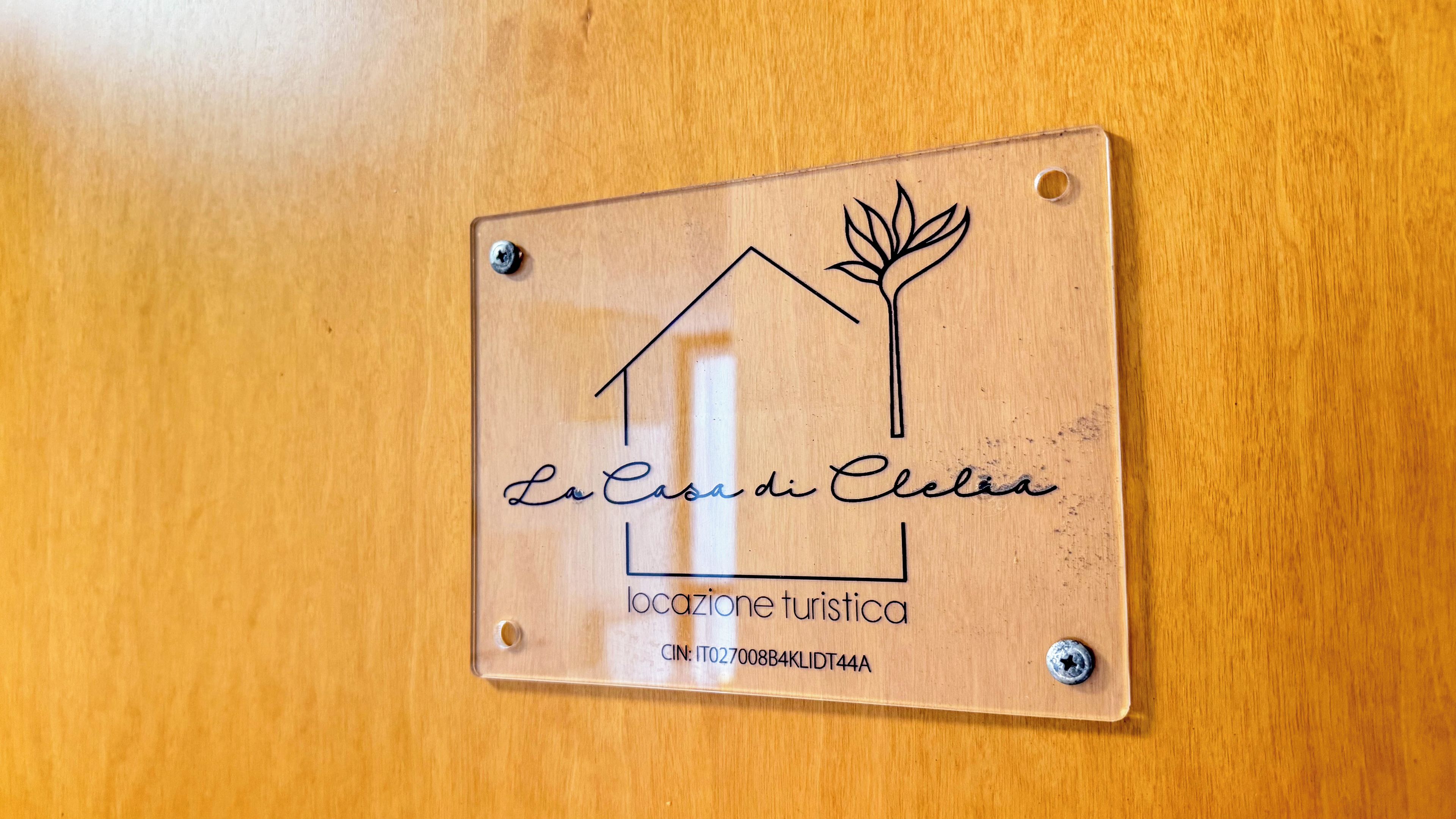 Una placa de madera con un símbolo de casa y hoja, 'La Casa di Celia', y el texto 'locazione turistica'.