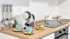 Una cocina moderna con una cocina por inducción negra, un hervidor y un juego de utensilios. Hay dos tazas azul claro y platos con comida sobre la encimera.
