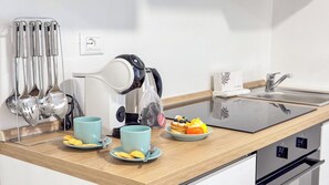 Una cocina moderna con una cocina por inducción negra, un hervidor y un juego de utensilios. Hay dos tazas azul claro y platos con comida sobre la encimera.