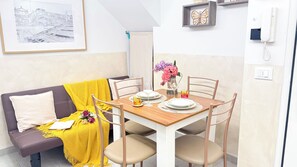 Uma área de jantar acolhedora com uma mesa de madeira posta para dois, um cobertor amarelo em um sofá marrom, e uma obra de arte emoldurada acima da mesa.