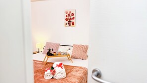 A hotel room with a bed, a bedside table with a lamp, a tray with fruits and a teapot, and towels with a rose decoration. - Sweet Apartment by Ca-sa Check (Chioggia)
