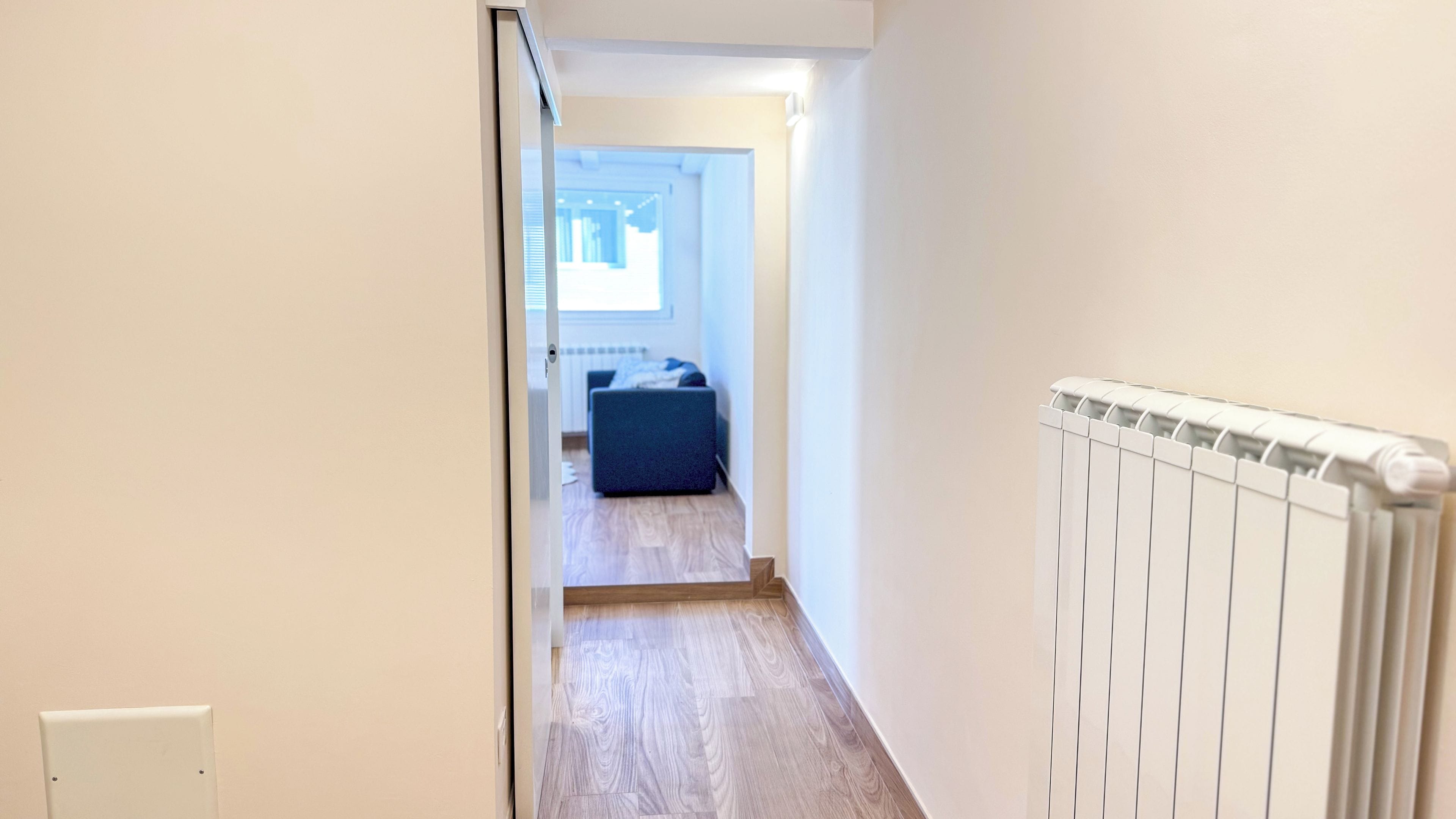 A narrow hallway with a radiator on the right and a blue sofa in the background.