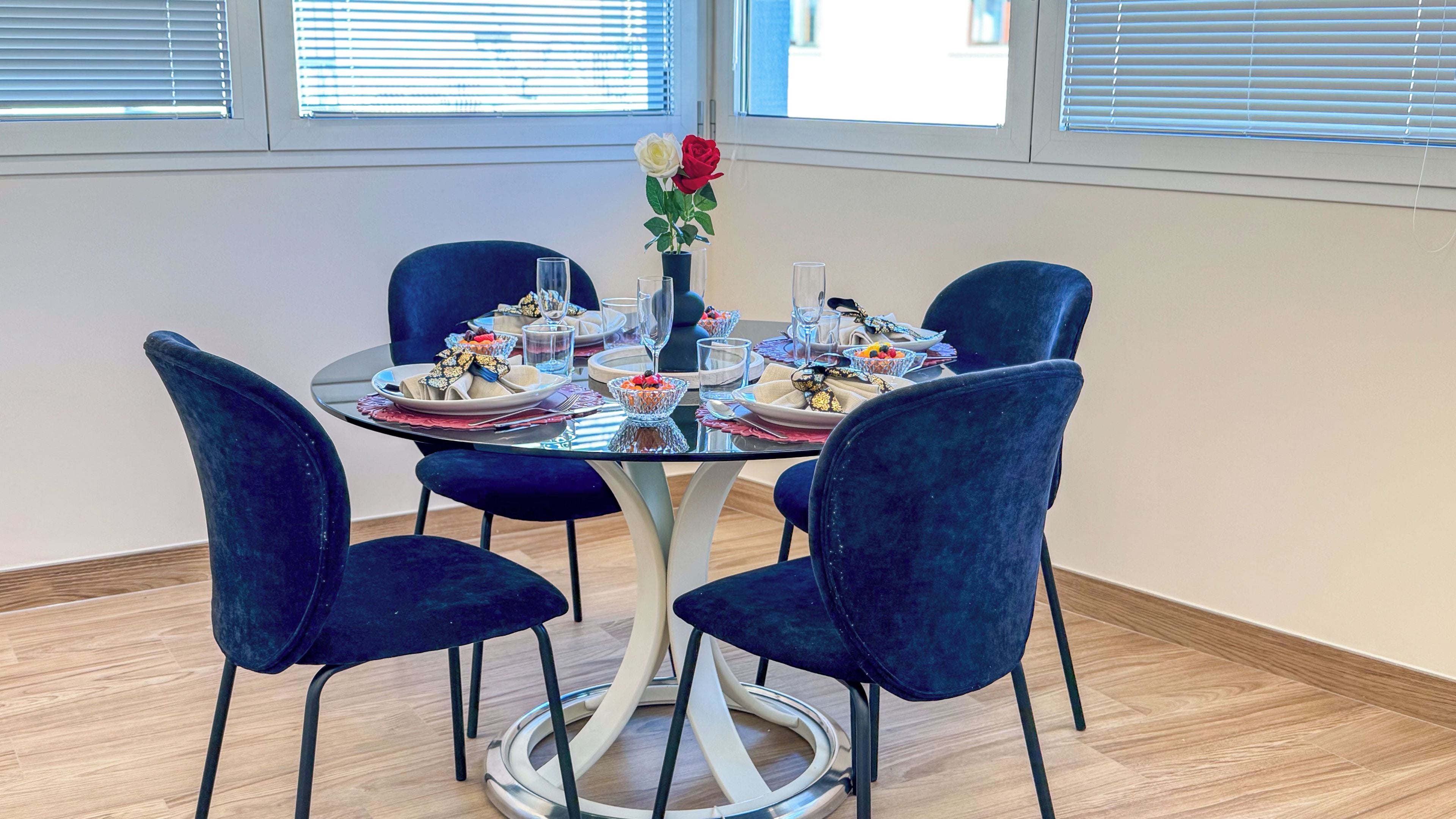 A dining table with four chairs, a vase with flowers, and a glass of water.