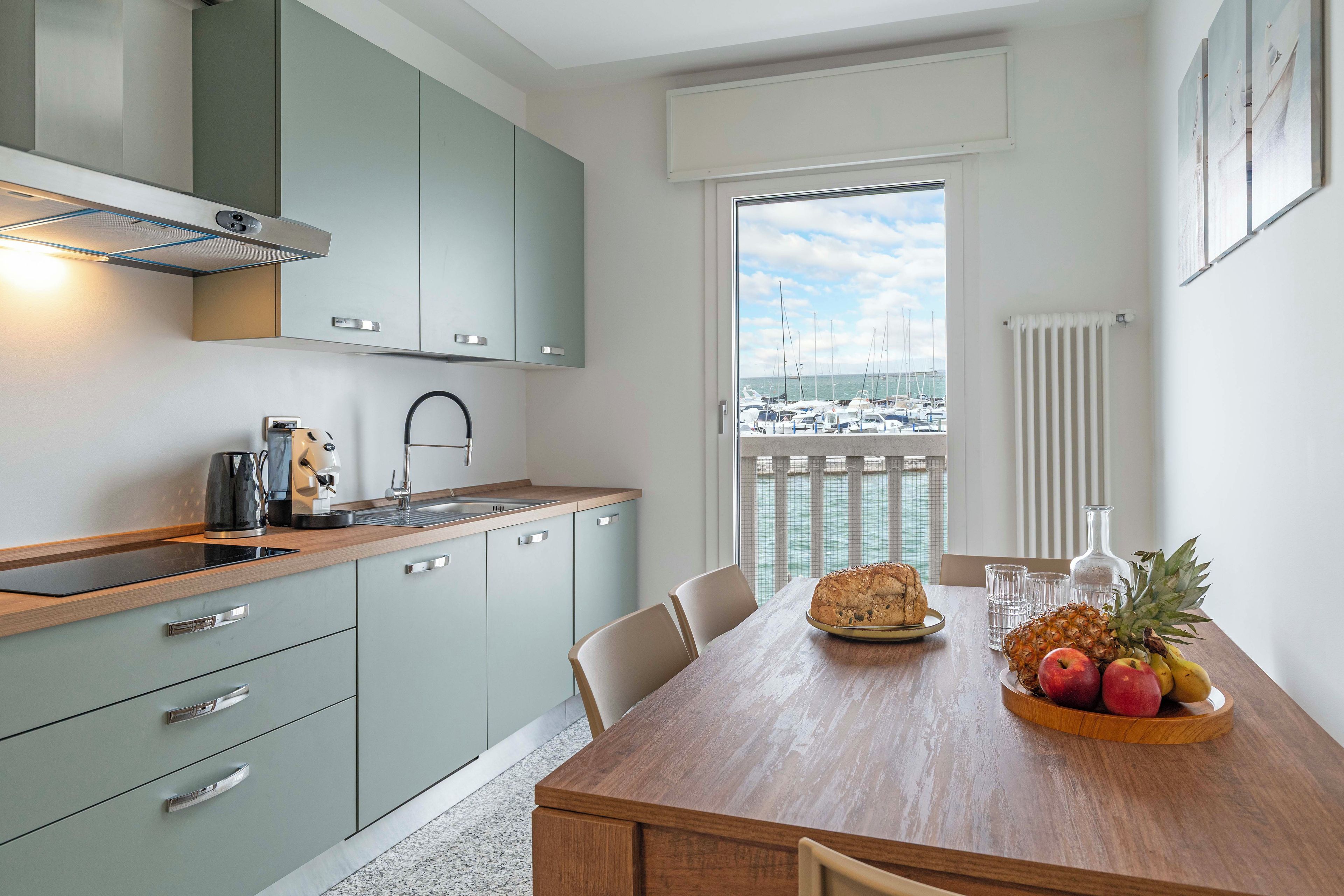 Una cocina moderna con encimera de madera, una mesa de comedor con sillas y vistas a barcos a través de un ventanal grande.