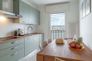 Una cocina moderna con encimera de madera, una mesa de comedor con sillas y vistas a barcos a través de un ventanal grande.
