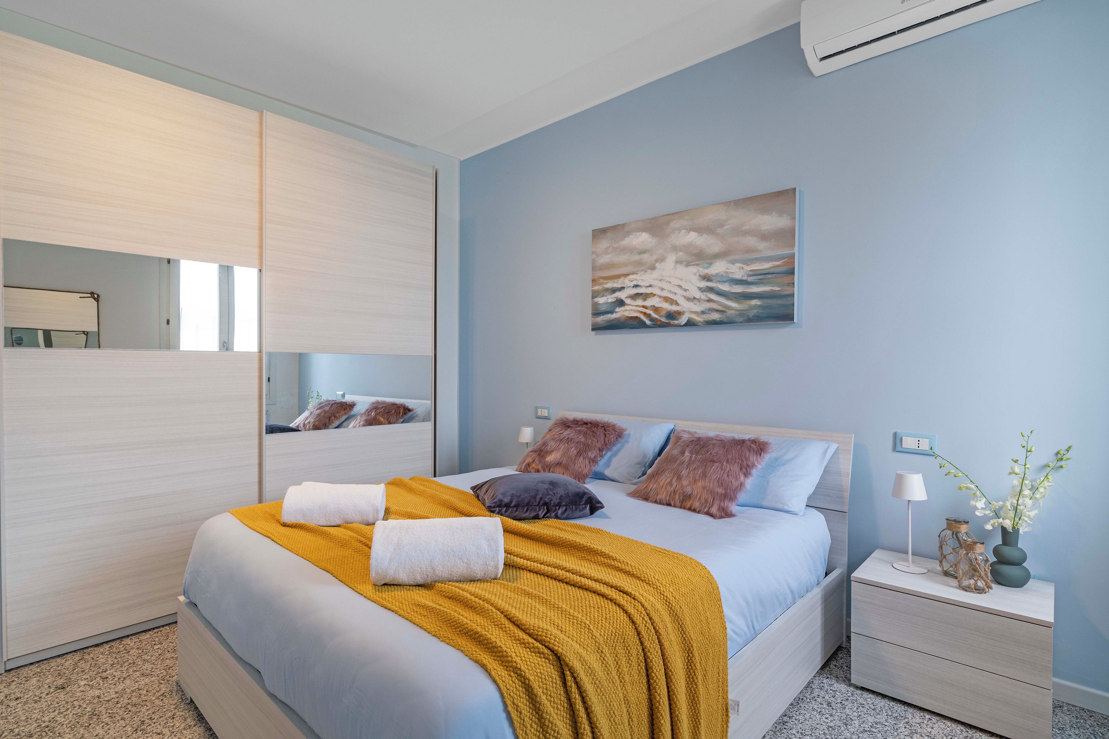 Un dormitorio con cama, mesita de noche, espejo y un cuadro en la pared.