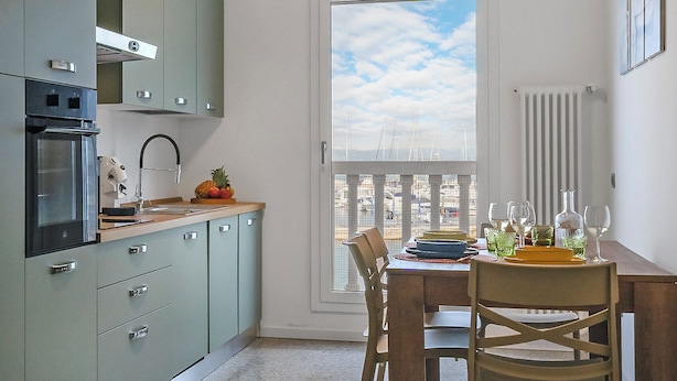 Uma cozinha compacta com área de jantar, vista para a marina através de uma janela ampla e um radiador na parede.