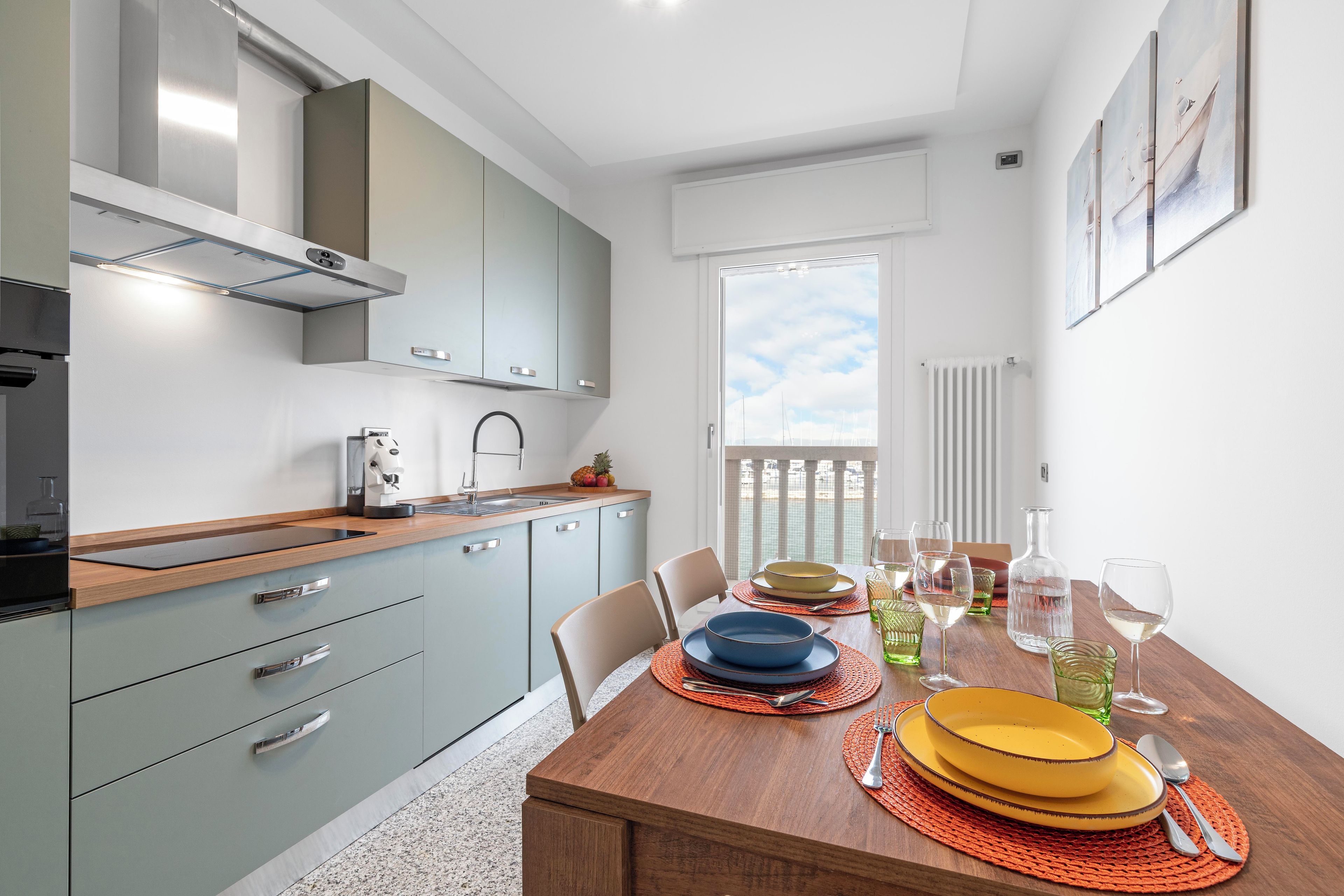 Una cocina moderna con armarios grises, encimera de madera y una mesa de comedor preparada para cuatro personas, con platos, vasos y cubiertos.