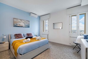 Un dormitorio con cama, ventana, radiador y vistas a la ciudad.