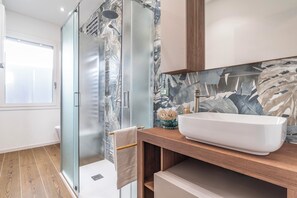 Un baño moderno con cabina de ducha de vidrio, un lavabo blanco y un mueble de tocador de madera.