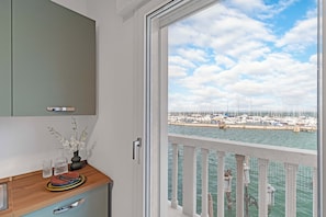 Quarto com vista para uma marina, balcão de madeira com um vaso de flores e uma porta branca.