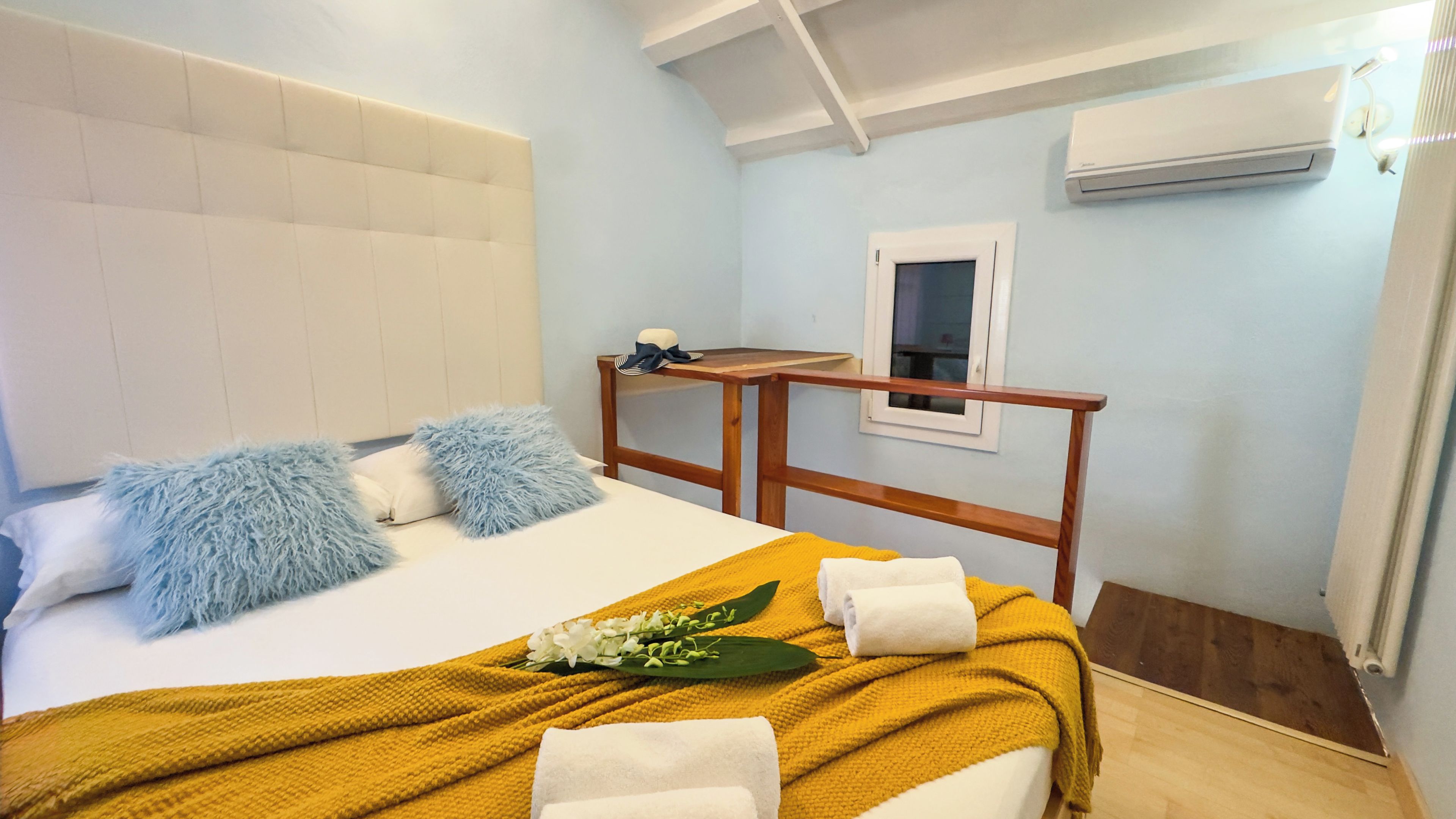 Une chambre d’hôtel avec un lit, une tête de lit en bois, une petite table, un appareil de climatisation et une fenêtre.