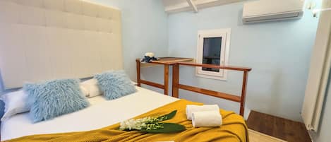 A hotel room with a bed, a wooden headboard, a small table, an air conditioning unit, and a window.