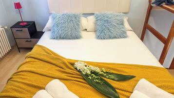 Un llit ben arropat amb almoades mullades i una manta de color mostassa, i un arranjament floral.