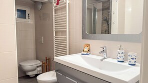 Ein Badezimmer mit einem weißen Waschbecken, zwei Wasserhähnen, einem Spiegel und einer Toilette.