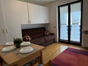 A modern living space with a dining area, a sofa, and a sliding glass door leading to a balcony. - Maison Letì Ca-sa Check (Aprica)