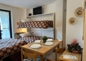 A compact hotel room with a bunk bed, a dining table set for two, and a small side table with a plant. - Maison Letì Ca-sa Check (Aprica)