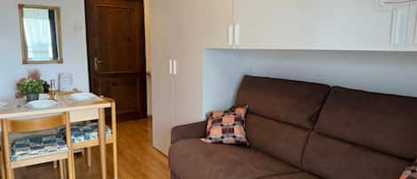 A cozy living room with a brown sofa, a wooden dining table with chairs, and a small table with decorative items.