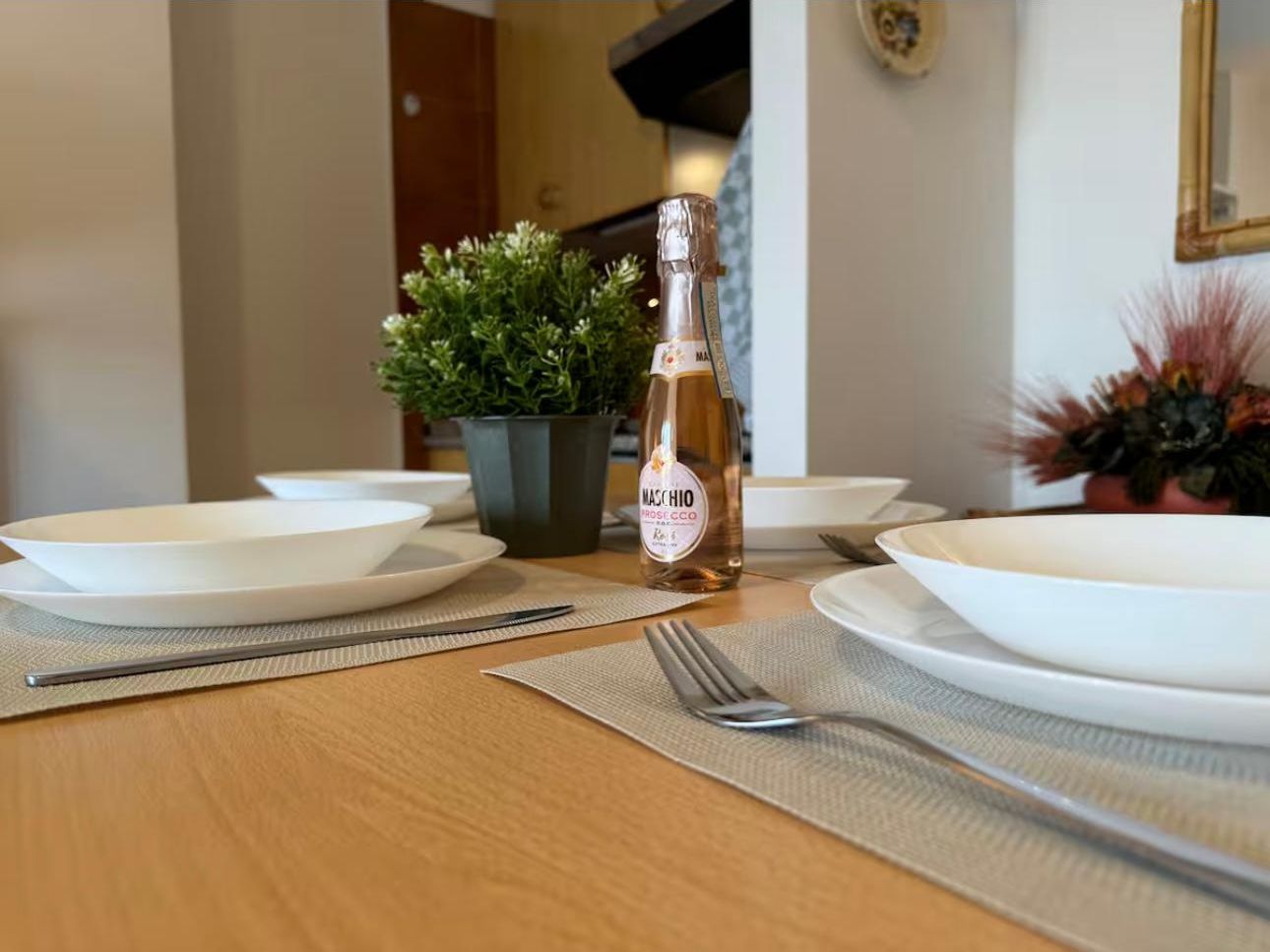 A dining table set with white plates, a bottle of Macchiato Rosé, and a small potted plant.