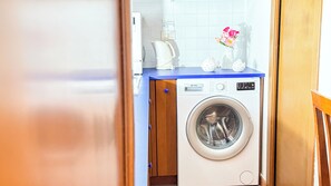 A compact laundry area with a front-loading washing machine, a small sink, and a coffee maker on a blue countertop. - Mar Suite by Ca-sa Check (Chioggia)