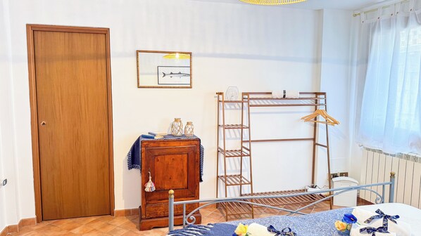 A room with a wooden door, a small cabinet, a metal drying rack, and a bed with a blue and white patterned bedspread. - Mar Suite by Ca-sa Check (Chioggia)