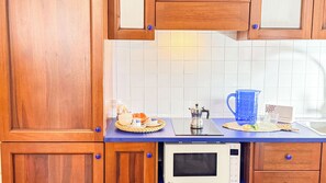 A kitchen with wooden cabinets, a microwave, a coffee maker, and a blue pitcher on the counter. - Mar Suite by Ca-sa Check (Chioggia)