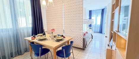 A dining area with a table set for two, chairs, a bottle of wine, and a vase with flowers.