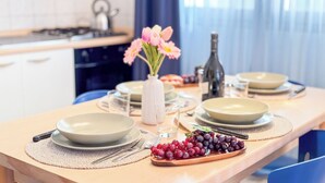 A dining table set with plates, cutlery, a vase of flowers, a bottle, and a bowl of grapes. - Liam & Leo Suite by Ca-sa Check (Chioggia)