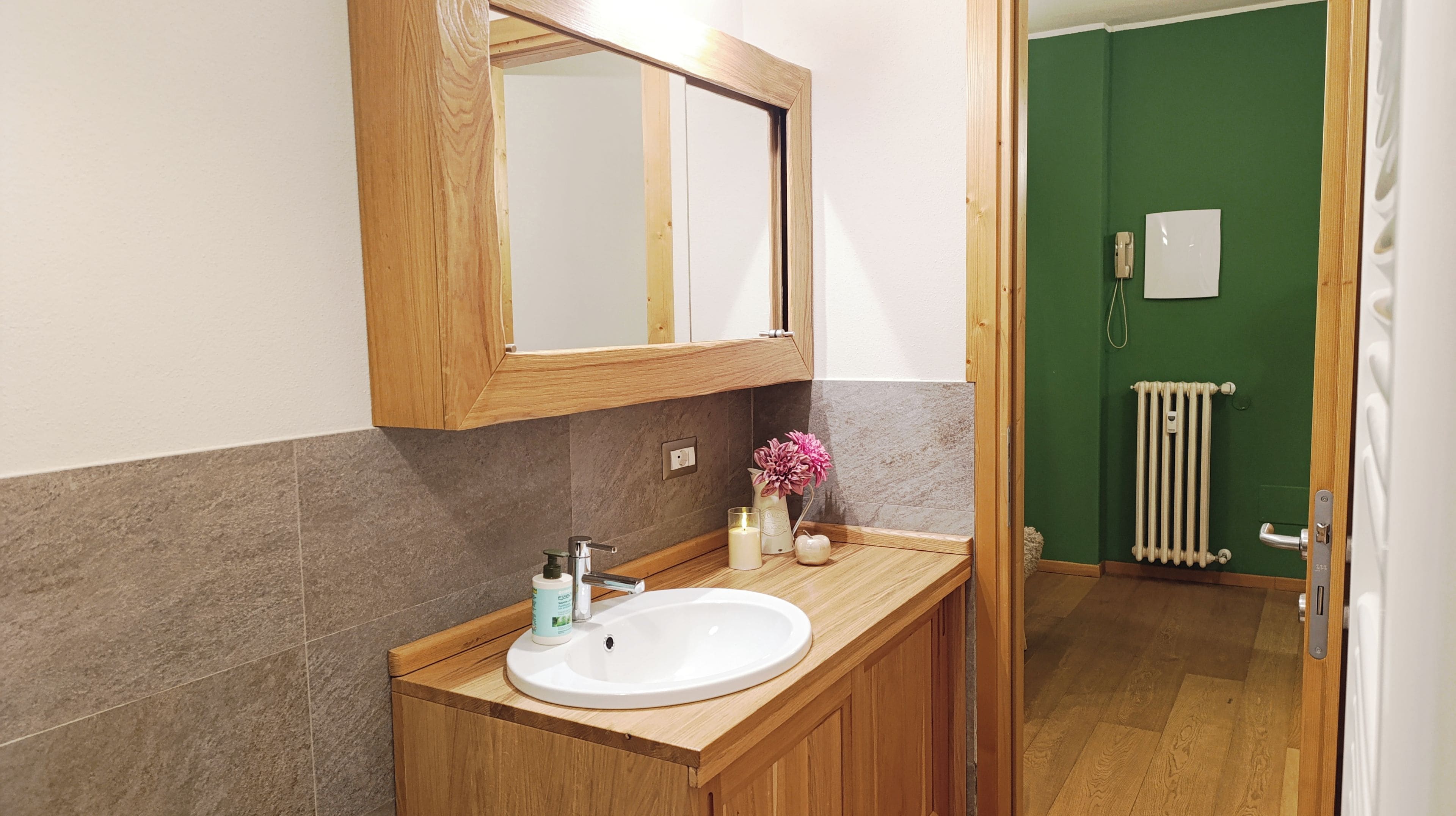 A bathroom with a wooden vanity, a white sink, a mirror, and a green door.