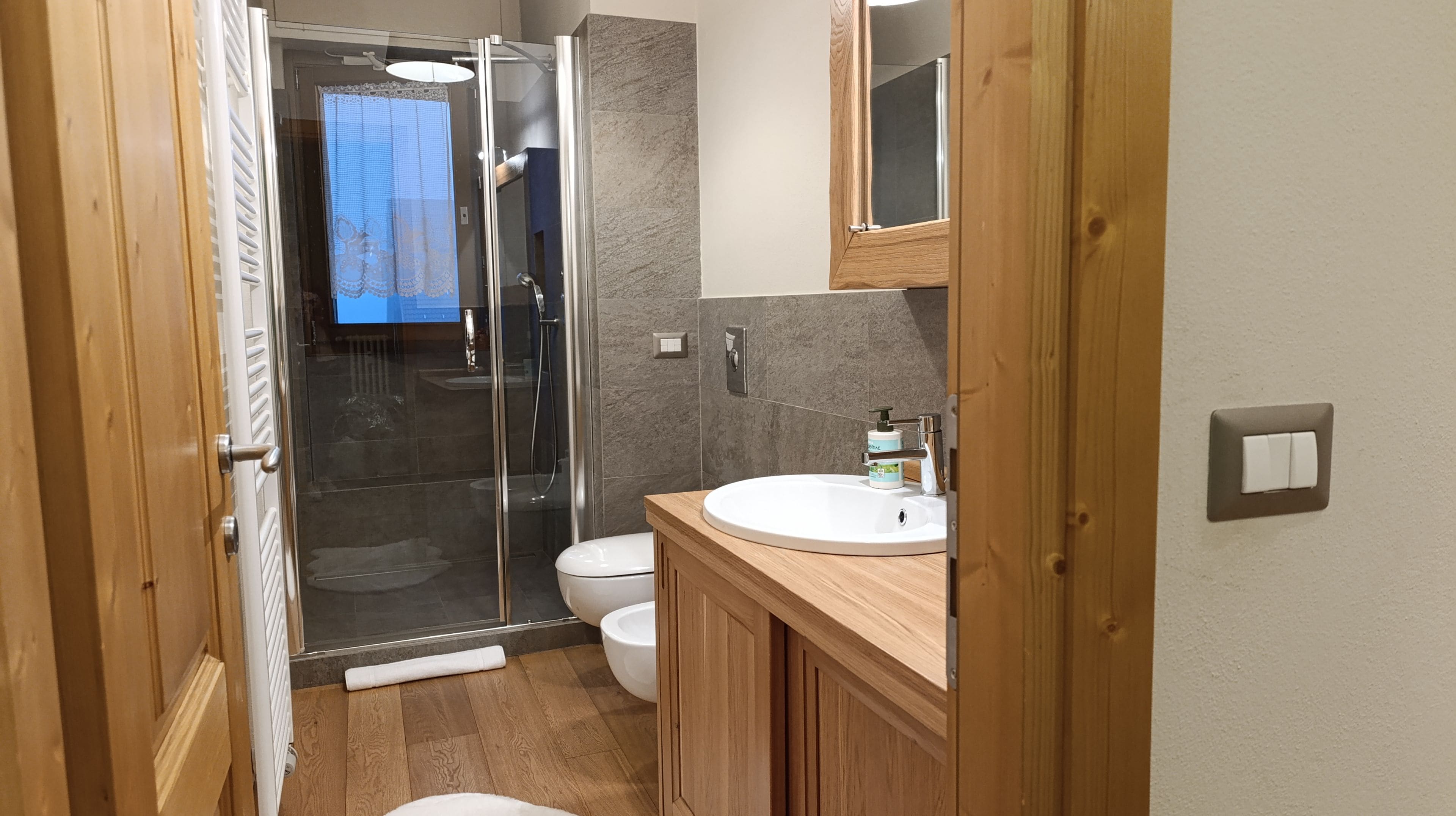 Un bagno moderno con cabina doccia in vetro, un water e un lavabo con mobile contenitore in legno.