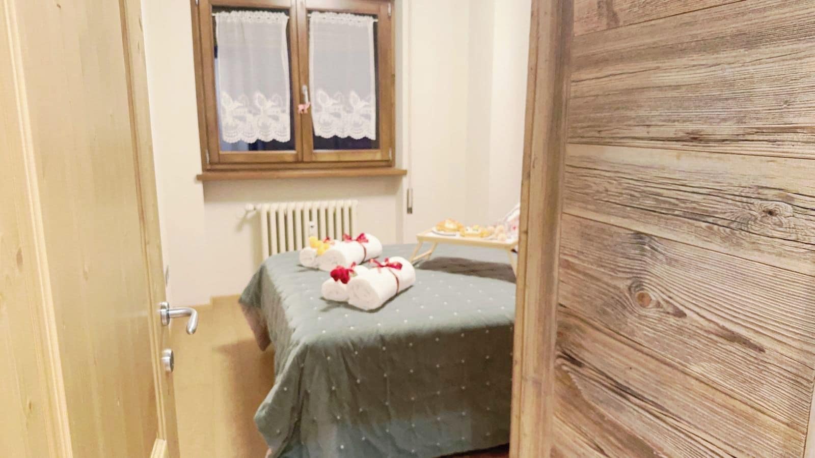 Une petite pièce avec un lit, une fenêtre ornée de rideaux en dentelle, un radiateur et une porte en bois.