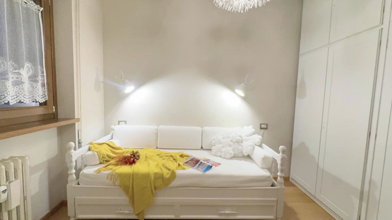 A white bed with a yellow blanket, white pillows, and a white headboard.