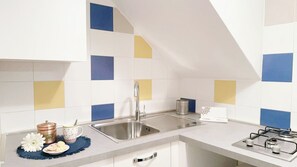 A kitchen with white cabinets, a stainless steel sink, a gas stove, and a blue and yellow tiled backsplash. - Appartamento Sestiere Castello by Ca-sa Check (Venice)