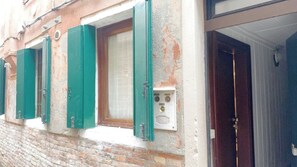 Eine Gebäudefassade mit Fenster und Tür, mit grünen Fensterläden und einem an der Wand montierten Stromkasten.