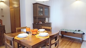 A dining area with a wooden table set for four, a cabinet with glass doors, and a bench with a patterned cushion. - Casa Savilla by Ca-sa Check (Vodo Cadore)