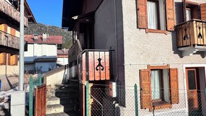 Um chalé tradicional com escadaria de madeira, varanda com grade de metal e montanhas ao fundo.