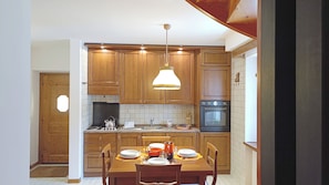 A compact kitchen with wooden cabinets, a gas stove, an oven, and a dining table set for four.