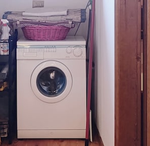 A white washing machine in a laundry room with a pink basket on top.