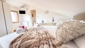 Una habitación de hotel con una cama, un almohadón mullido, una toalla enrollada y un televisor fijado a la pared.