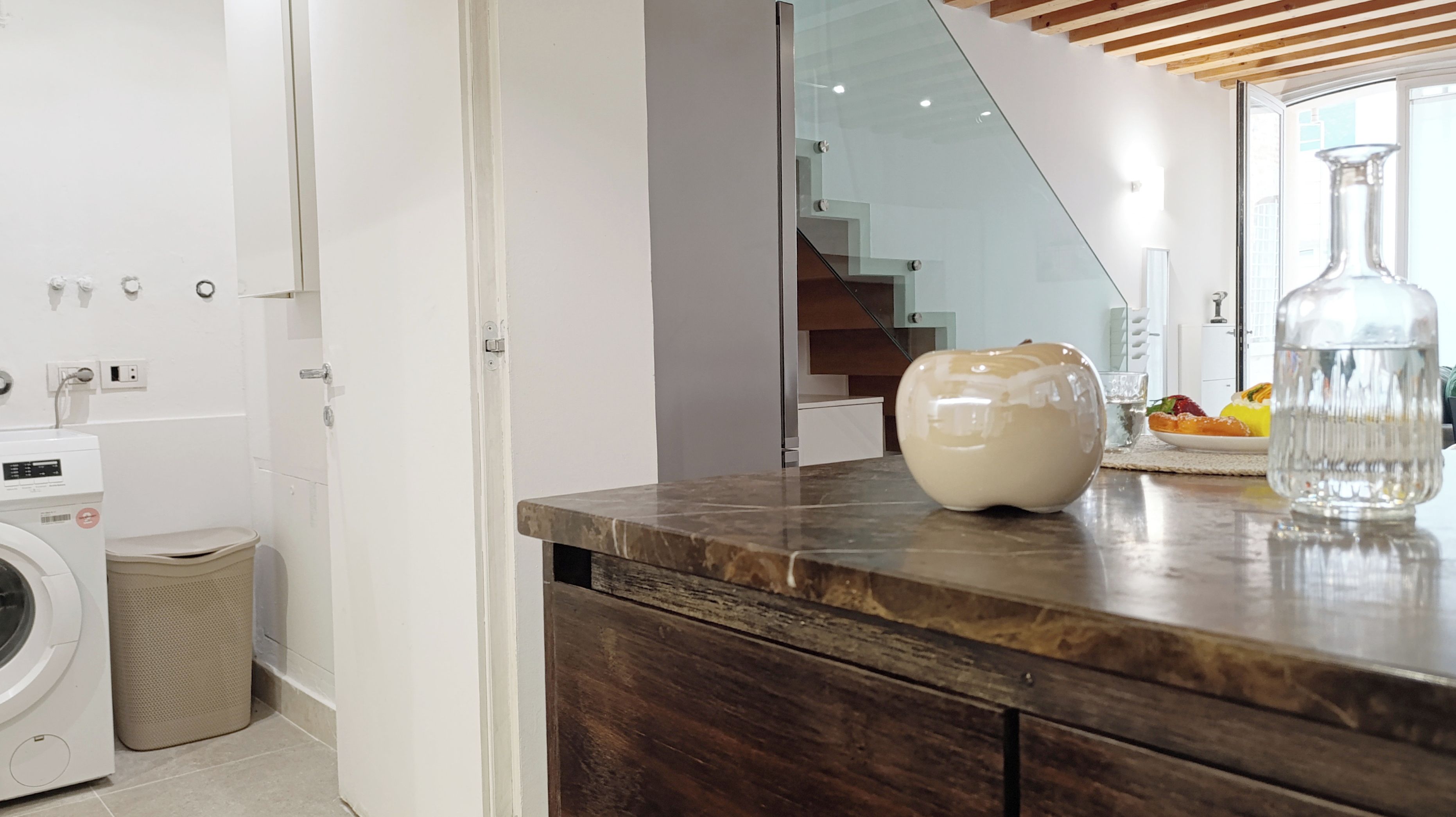 Cozinha moderna com bancada de mármore, máquina de lavar e um vaso de vidro.
