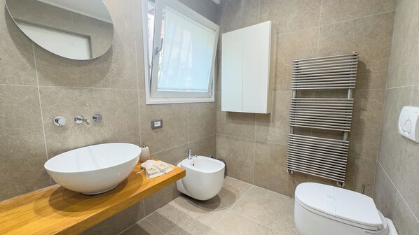 A bathroom with a large white basin, a small white toilet, a towel dispenser, and a towel rack.