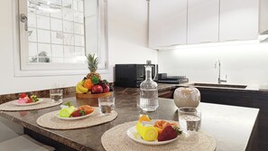 A modern kitchen with a marble countertop, a fruit bowl, a coffee maker, and a sink.