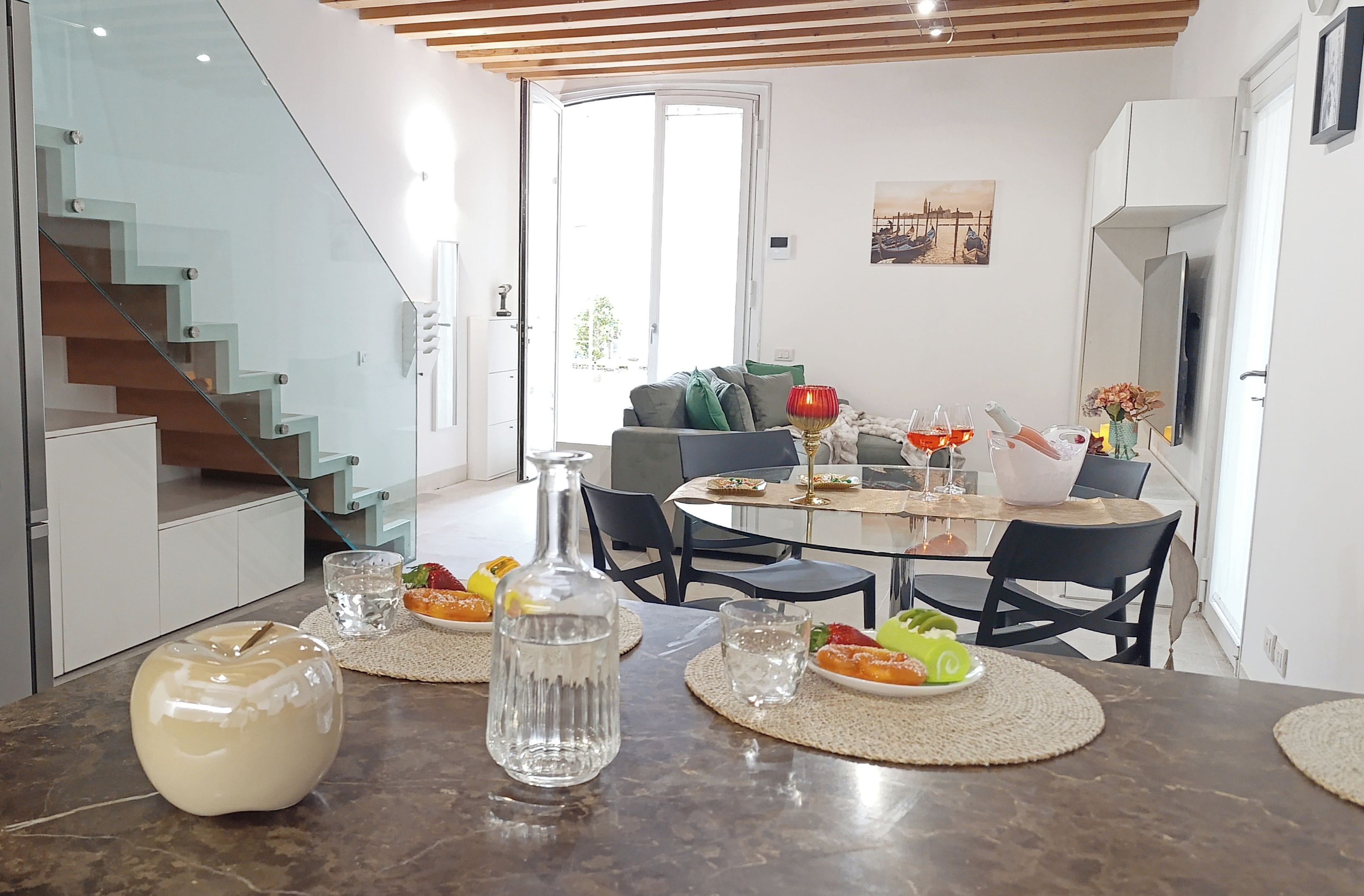Et moderne spiseområde med en glas trappe, et spisebord dækket med mad, og en sofa i baggrunden.