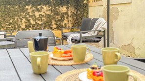 A table with green mugs, a small pot, and a plate of fruit.