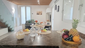 Cozinha moderna com bancada de mármore, mesa de jantar posta para quatro pessoas e uma fruteira com abacaxi, uvas e laranjas.